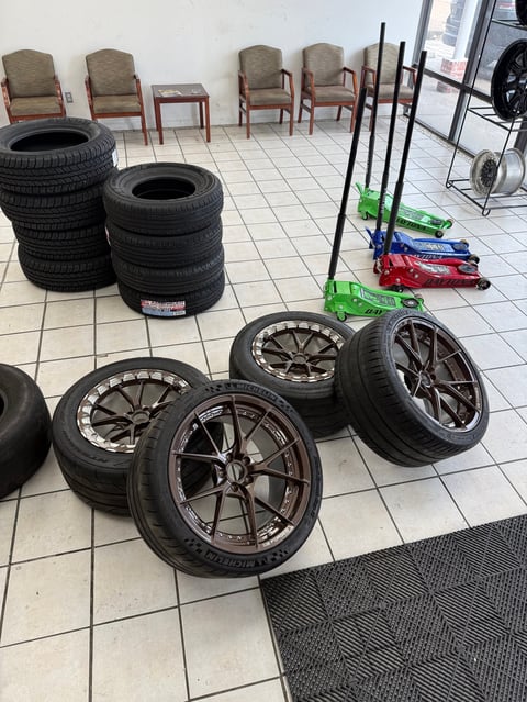 Car wheels and tires displayed on white tile floor in automotive shop
